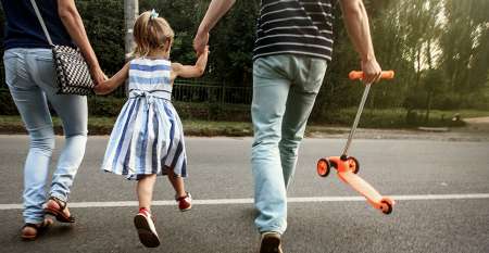 Parents holding their little girl's hand crossing road to park