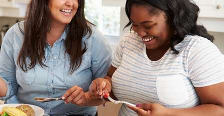 Two happy women eating in kitchen Two happy women eating in kitchen