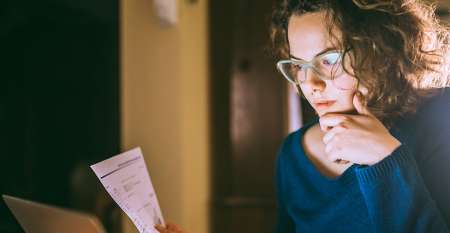 Young woman holding paper staring at laptop screen Young woman holding paper staring at laptop screen