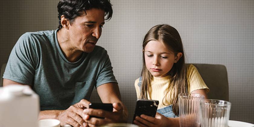 Dyn a merch ifanc yn edrych ar ffonau symudol