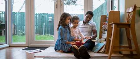 Man and two young children sitting on floor reading