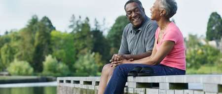 Older couple sitting talking on jetty over lake 