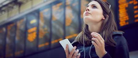 Young woman in front of departure board holding phon