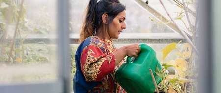 young-woman-watering-plants-in-greenhouse