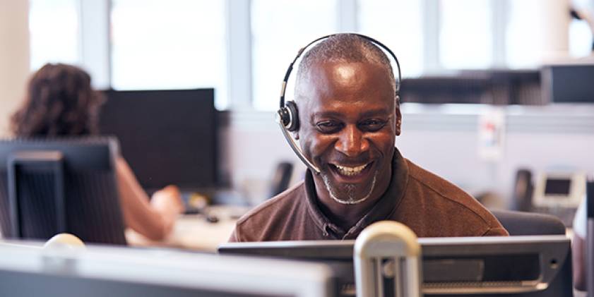 Dyn yn gwisgo clustffonau yn ffonio ar gyfrifiadur